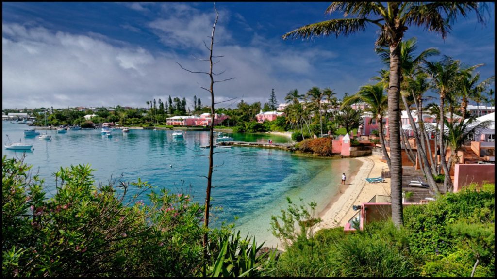 A beach with people swimming in it and buildings on the shore.