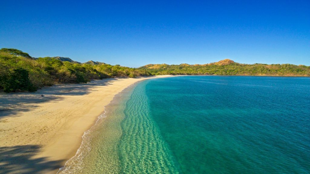 A beach with a body of water and mountains in the background.