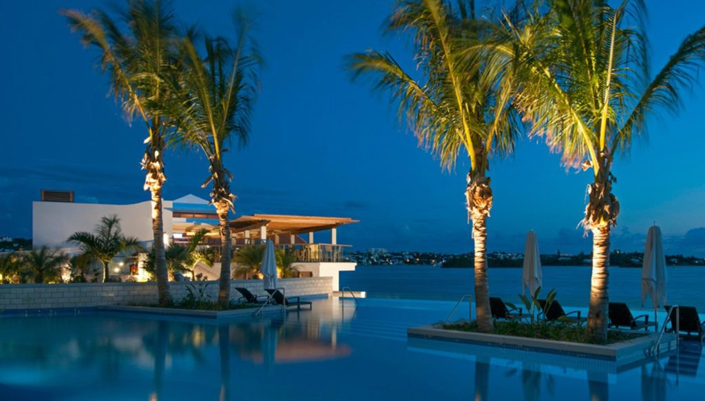 A pool with palm trees and chairs in the water.