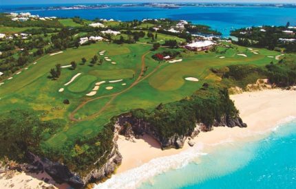 A golf course with a sandy beach and ocean.