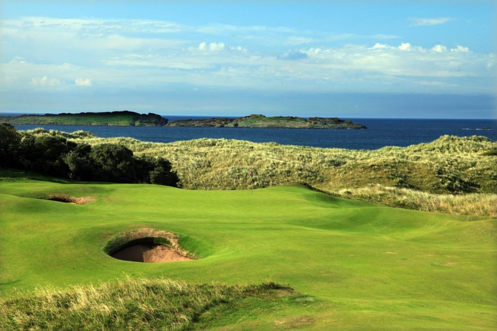 A golf course with green and sand on the side.