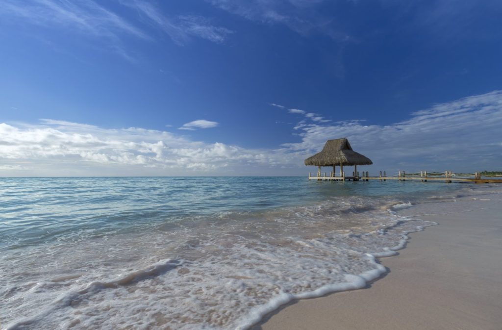 A beach with waves and an umbrella in the water.