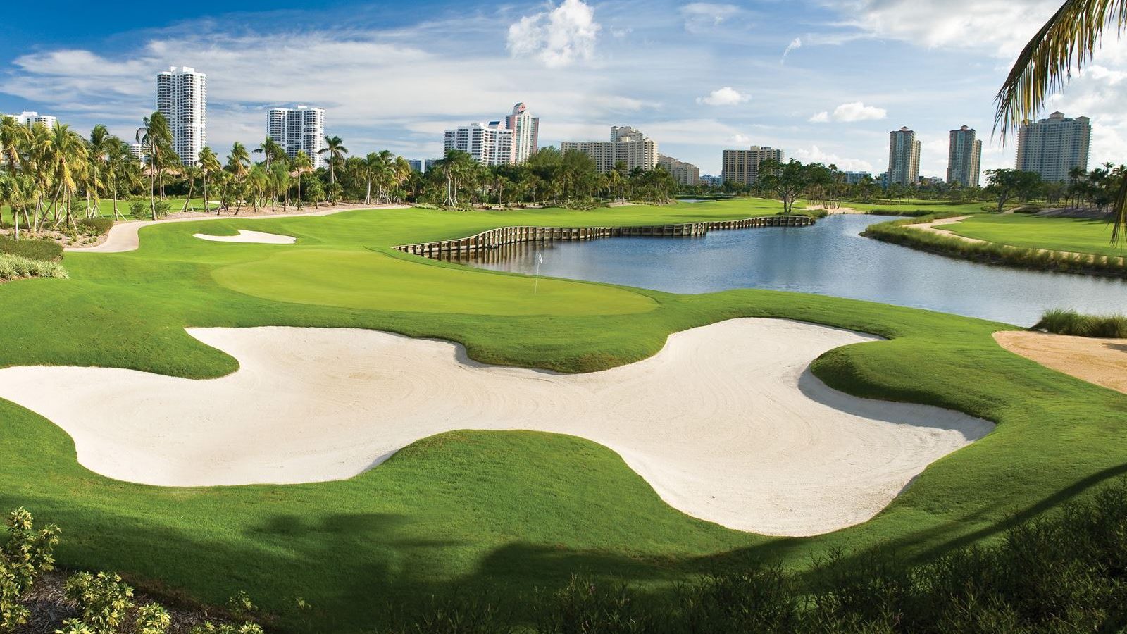 A golf course with many green areas and buildings in the background.