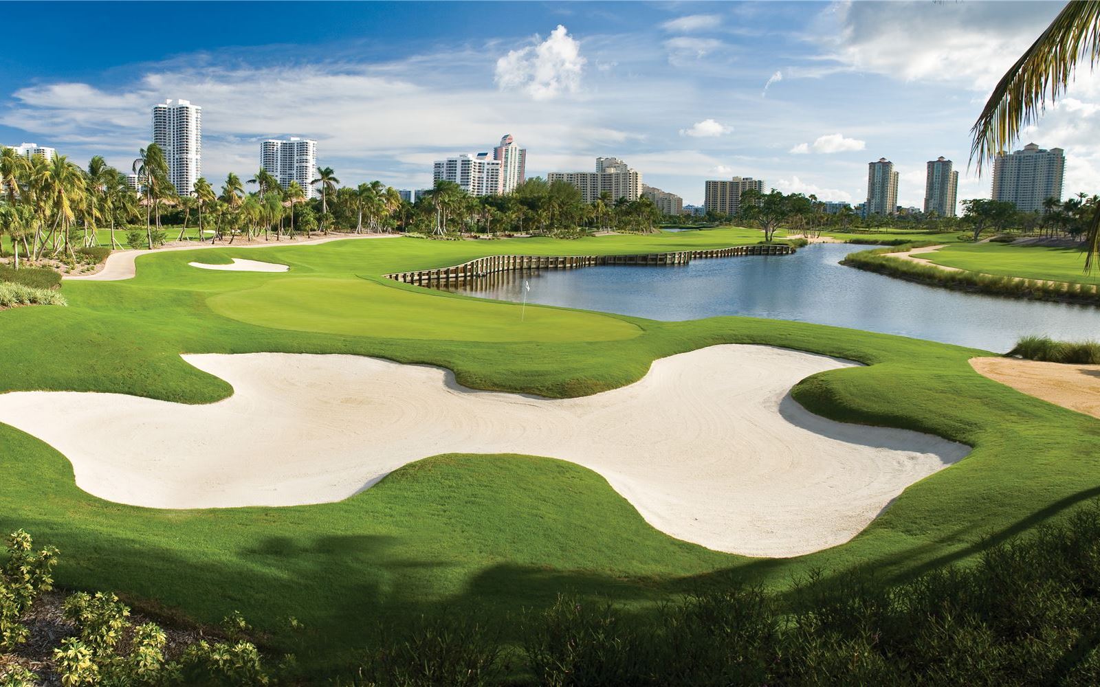 A golf course with many green areas and buildings in the background.