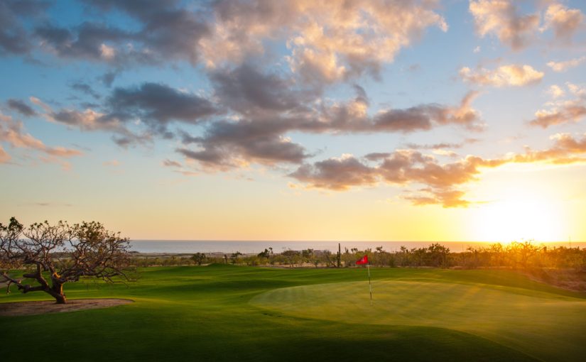 A golf course with the sun setting in the background.