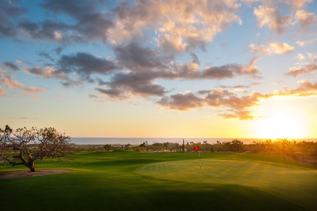 A golf course with the sun setting in the background.