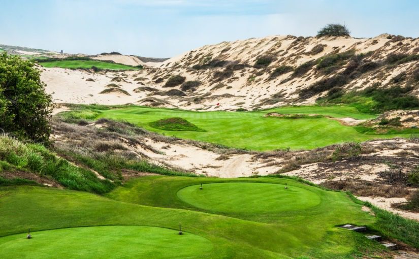 A golf course with sand dunes and green grass.