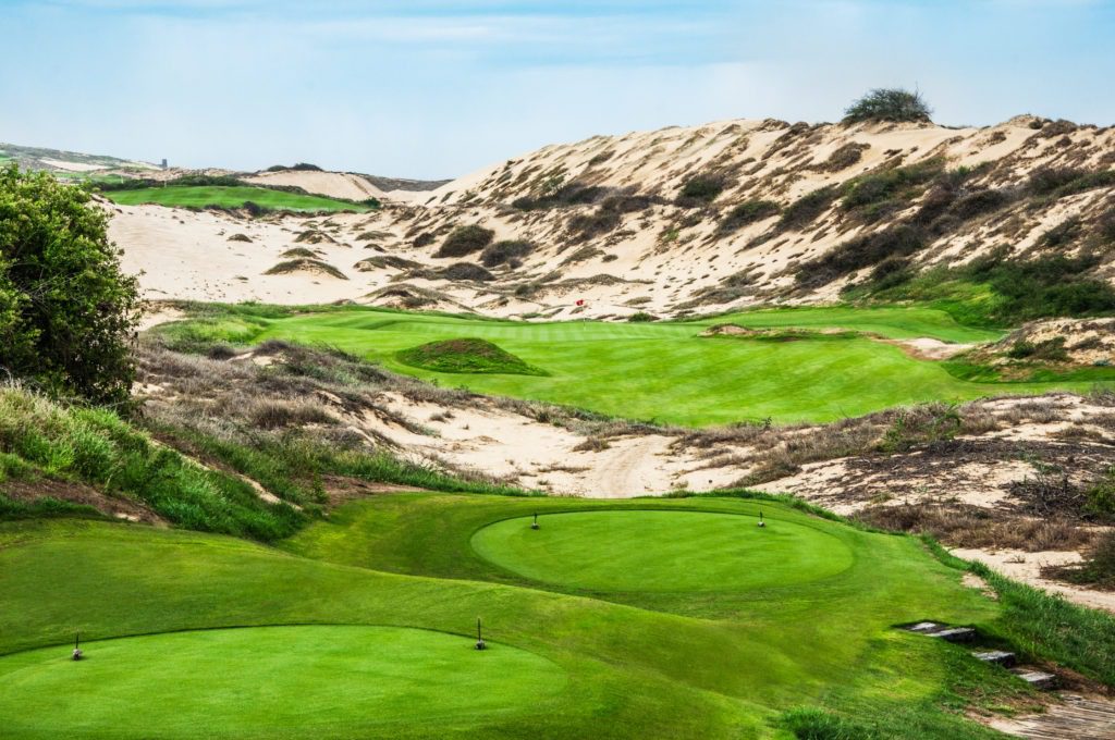 A golf course with sand dunes and green grass.