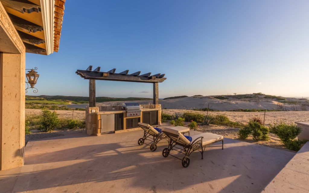 A beach with two lawn chairs and an outdoor grill.