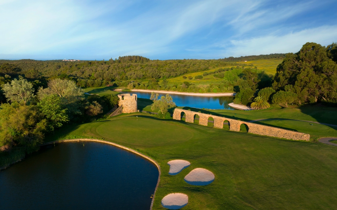 Golf course with a stone tower and lake.